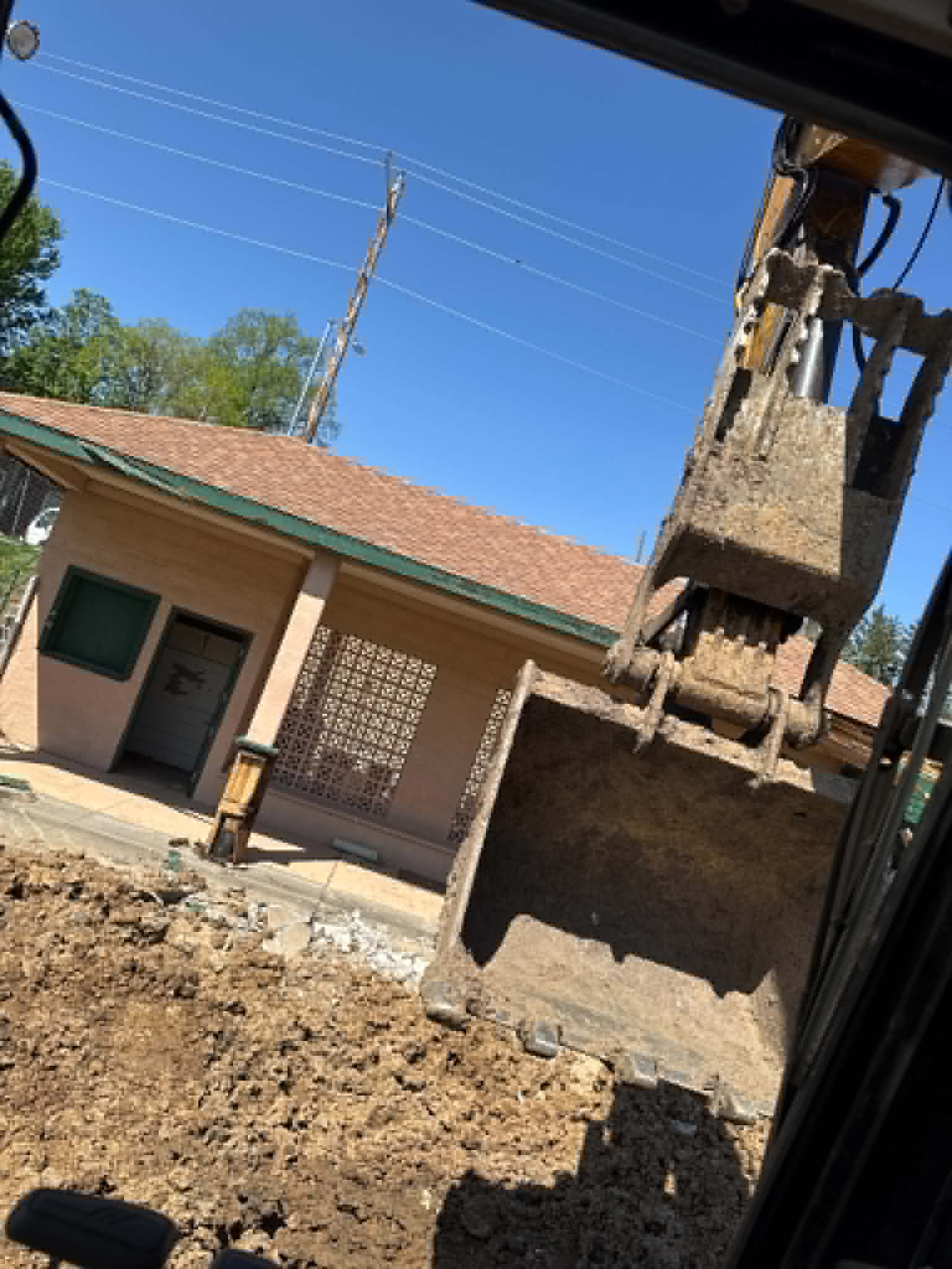 Excavator bucket clearing dirt in front of a single-story building during a local demolition project